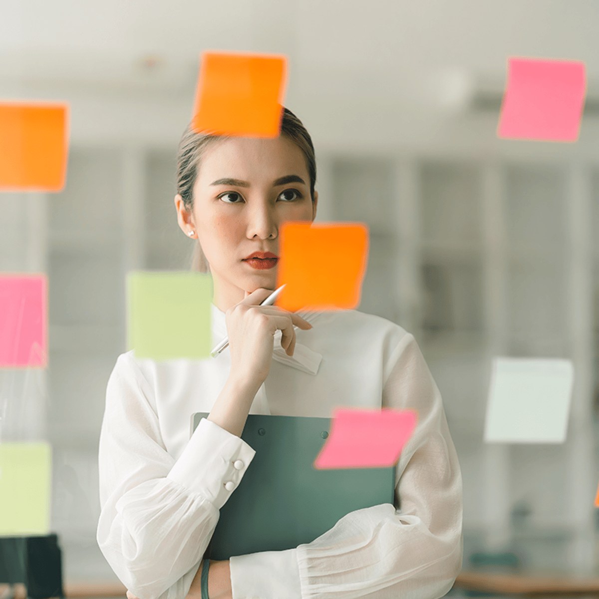 An employee standing behind a glass wall covered in colourful sticky notes, holding a clipboard — official image for Microsoft's Project Management Principles