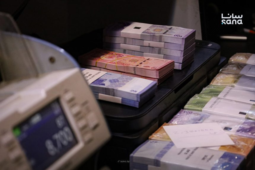 A cash-counting room with bricks of Syrian pound banknotes and a counting machine